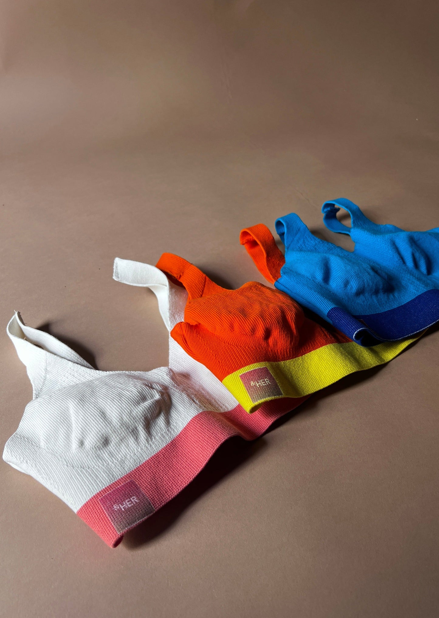 &HER color block bralette collection in cream, safety orange, and LED blue.